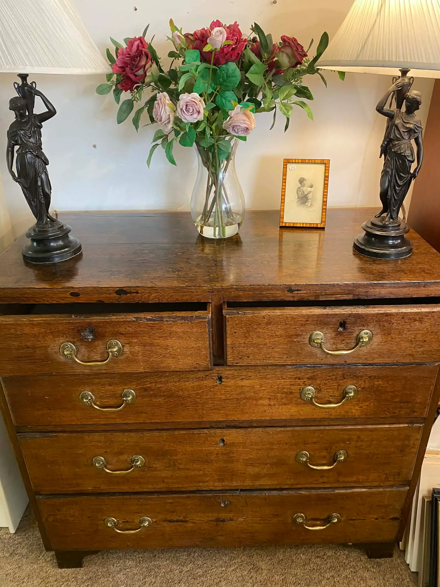 An antique oak chest of drawers dressed with bronze figurine lamps and fresh roses — typical of the quality pieces at Bridge Antiques Centre